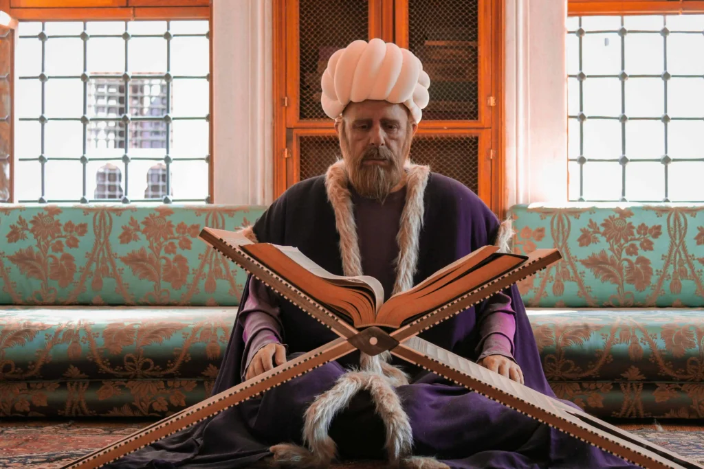 Kabbalista Ezra sentado diante de um livro sagrado aberto, usando vestes tradicionais e turbante branco, representante espiritual do mês hebraico de Tamuz.