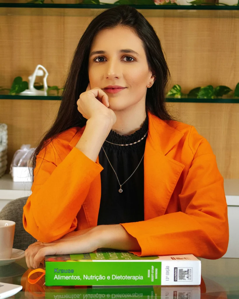 Kabbalista Leah sentada em ambiente de estudo, usando blazer laranja, representante espiritual do mês hebraico de Elul.