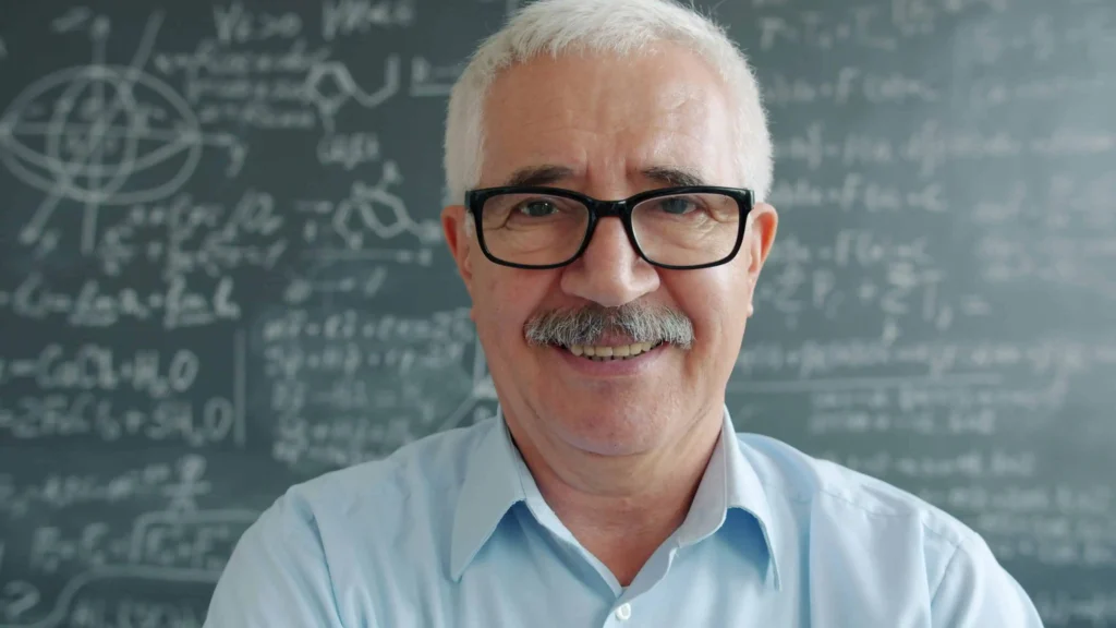 Kabbalista Moshe sorrindo diante de quadro com estudos e fórmulas, representante espiritual do mês hebraico de Elul.