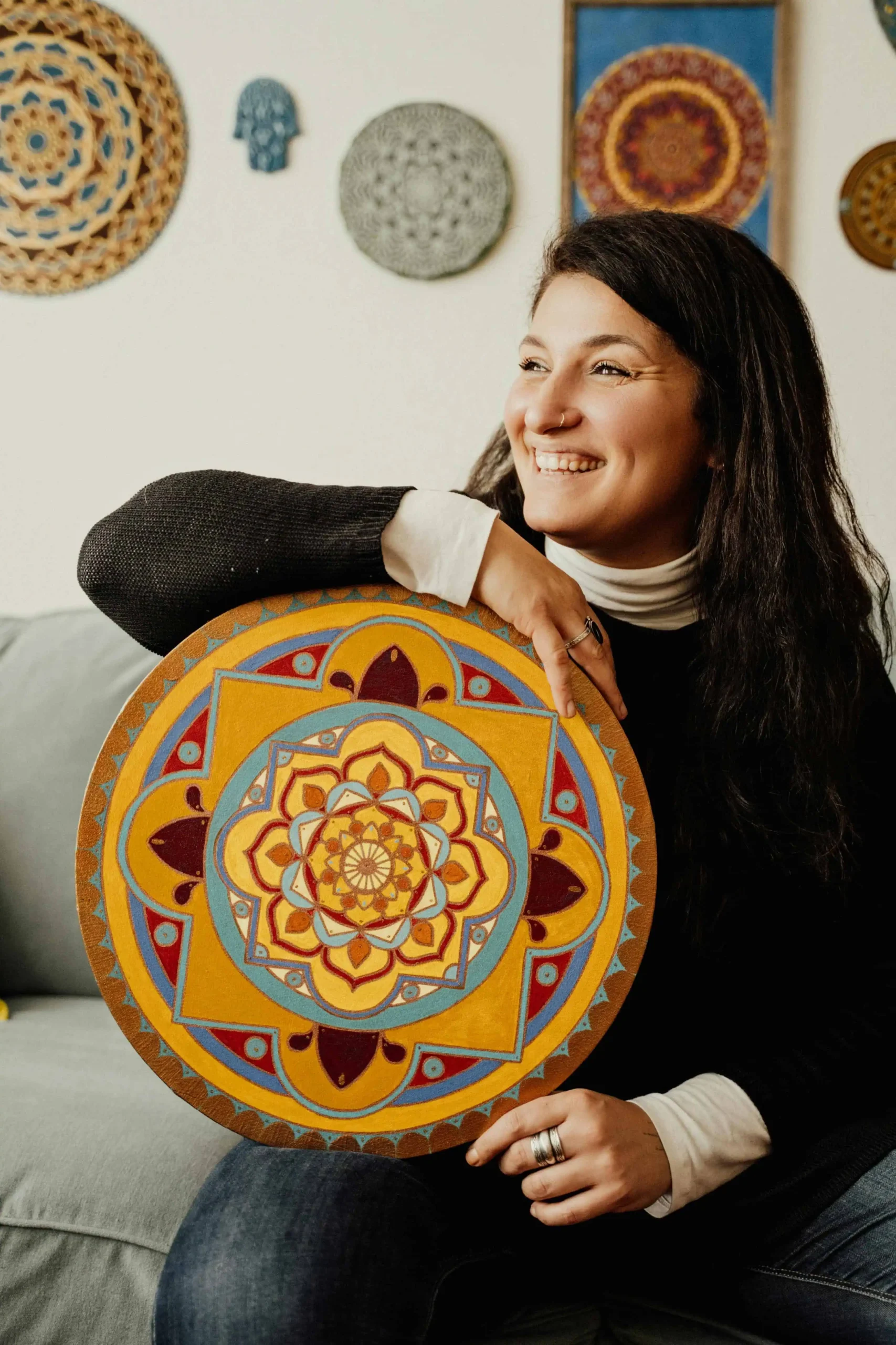 Kabbalista Zipporah sorrindo enquanto segura um mandala espiritual colorido em ambiente aconchegante e místico.